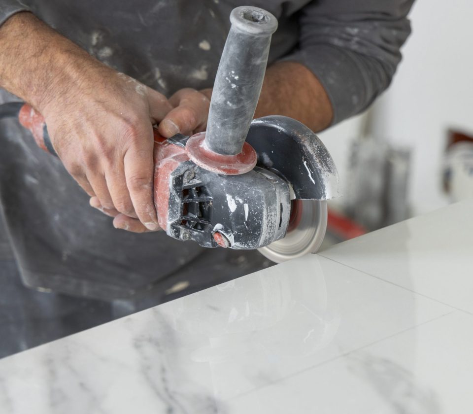 Craftman in grey shirt cuts a gray marble tile using an angle gr